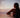 A woman in a pink bikini top sits at the edge of an infinity pool overlooking a sunset over the ocean, with palm trees silhouetted in the background.