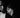 Black and white close-up portrait of a man and woman in formal evening wear, with the man wearing a tuxedo jacket and bow tie and the woman smiling near his face against a dark background.