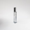 Clear glass 'Leather Noir' perfume bottle with silver cap on a light gray background