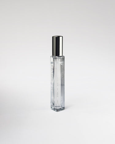 Clear glass 'Leather Noir' perfume bottle with silver cap on a light gray background