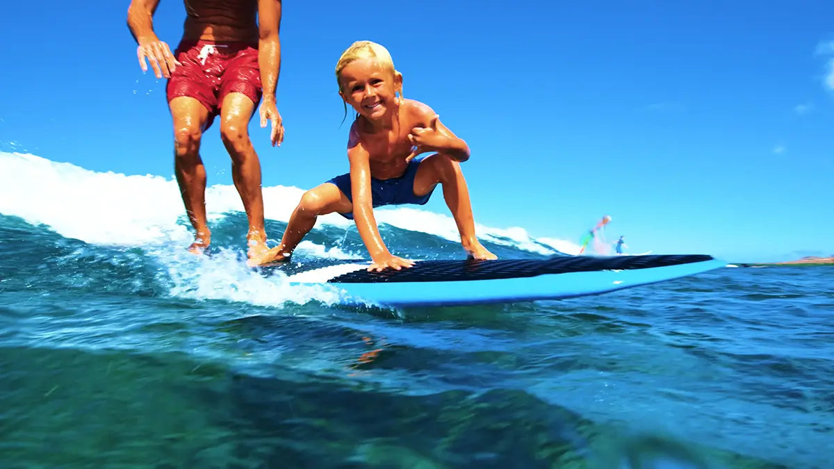 Child learning to surf with a instructor on a wave.