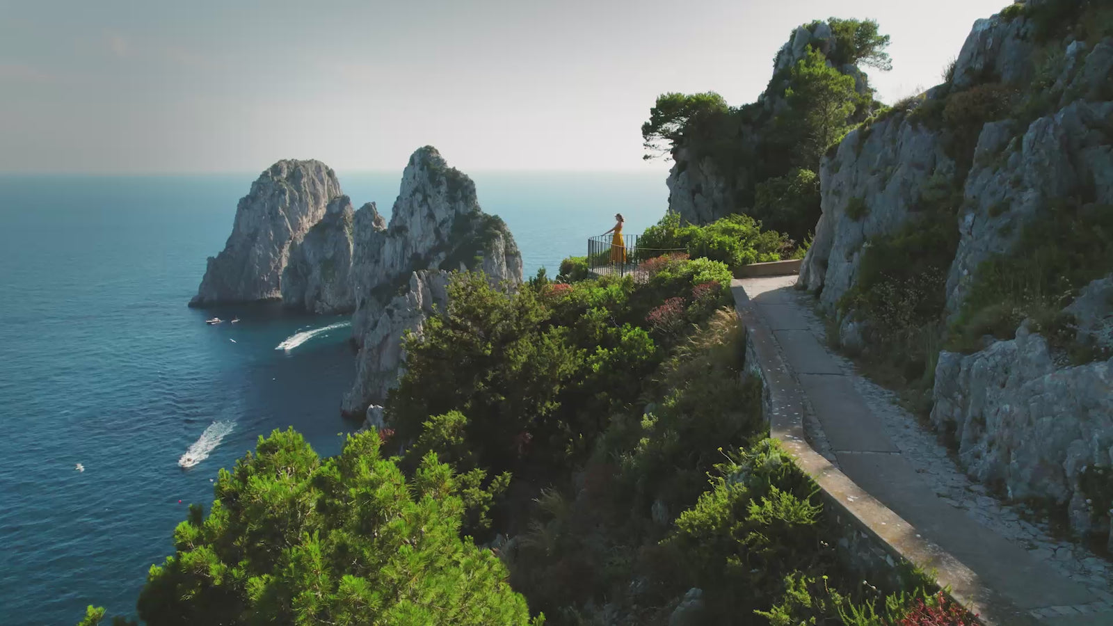 Elegant woman dressed in capri overlooking faraglioni rocks and coastal water