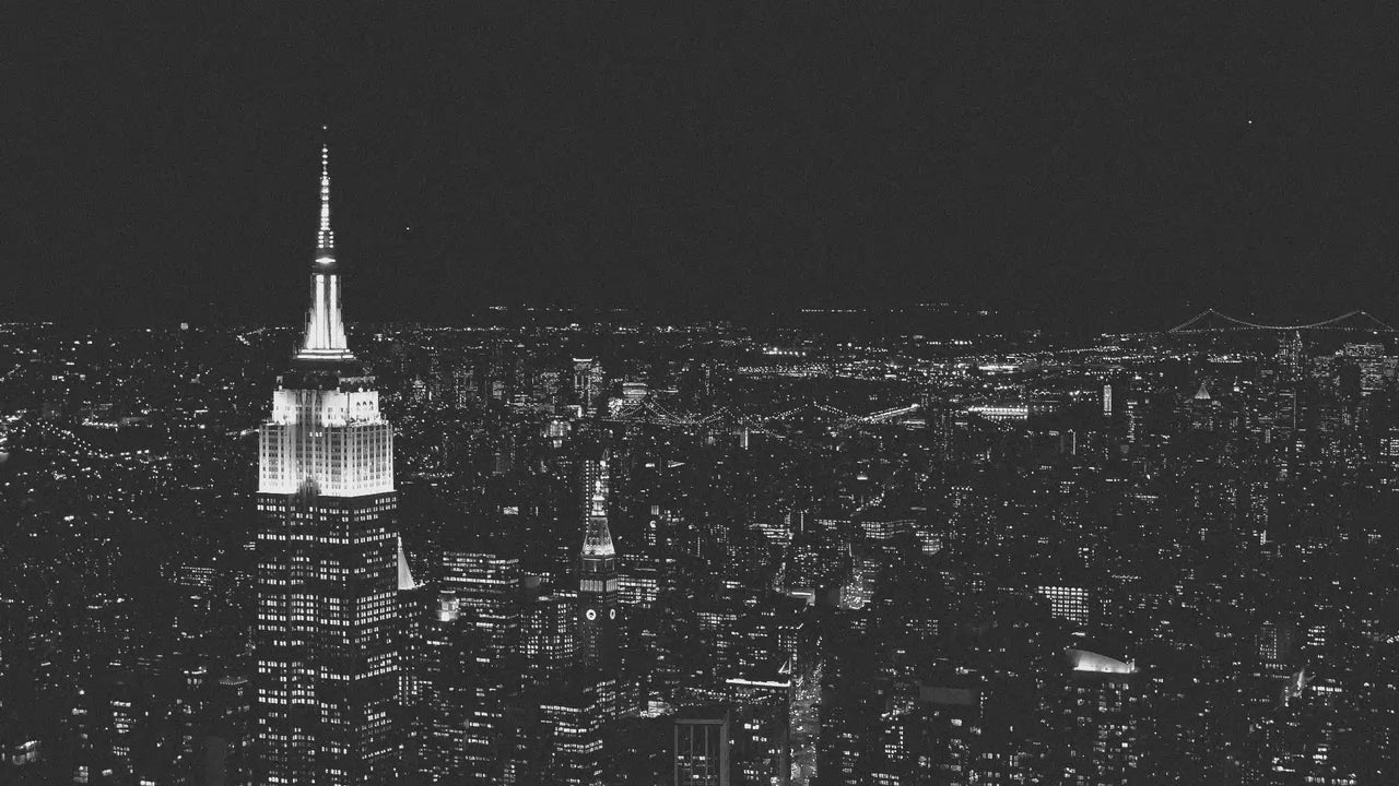 Aerial view of a cityscape at night with illuminated buildings, including the Empire State Building.