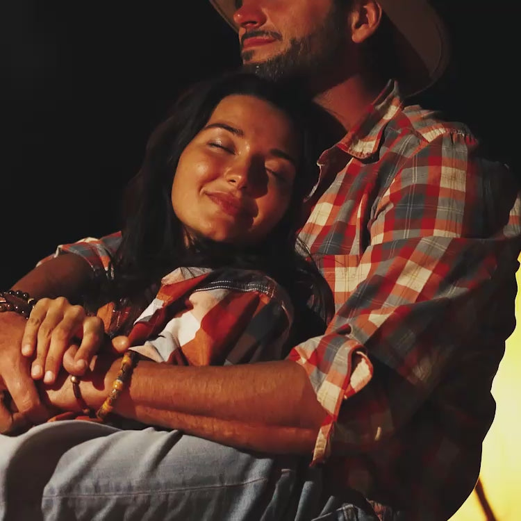 Two people in cowboy attire embracing against a dark background